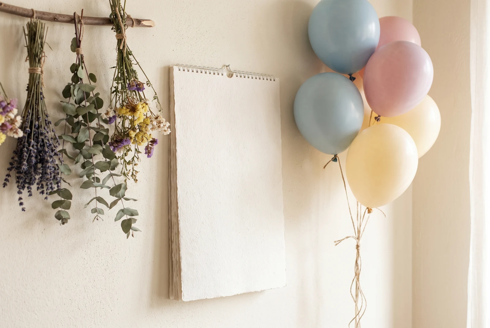 Imagen ilustrativa: mesa con calendario en blanco, globos pastel y flores secas